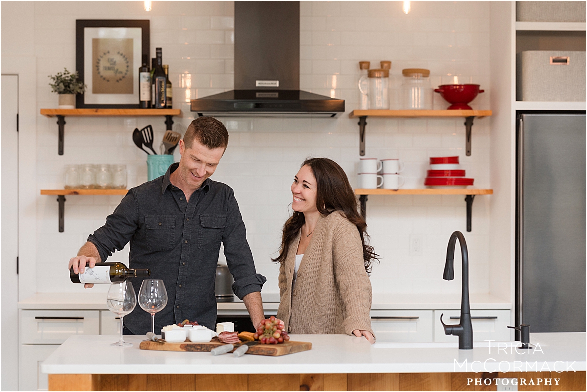 Man pours wine while talking with wife in kitchen